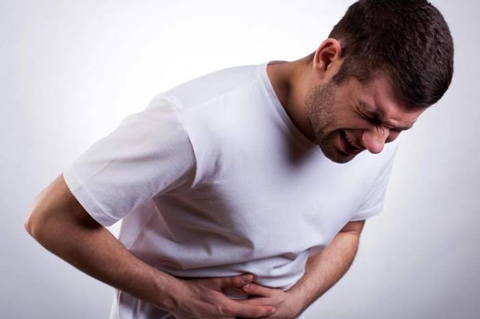 man-in-white-shirt-with-stomach-pain-against-gray-background