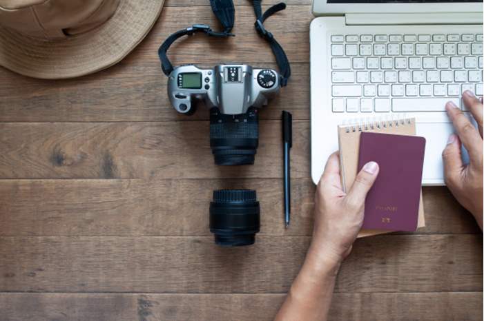 overhead-view-man-hands-using-laptop-holding-passport-camera-wooden-background_1428-2742