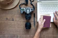 overhead-view-man-hands-using-laptop-holding-passport-camera-wooden-background_1428-2742